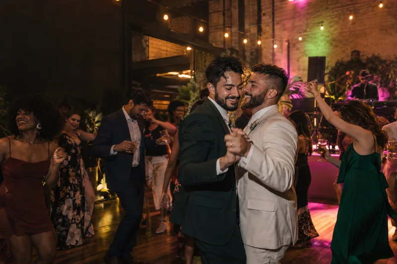 Imagem ilustrativa de dois noivos e convidados dançando em uma festa de casamento